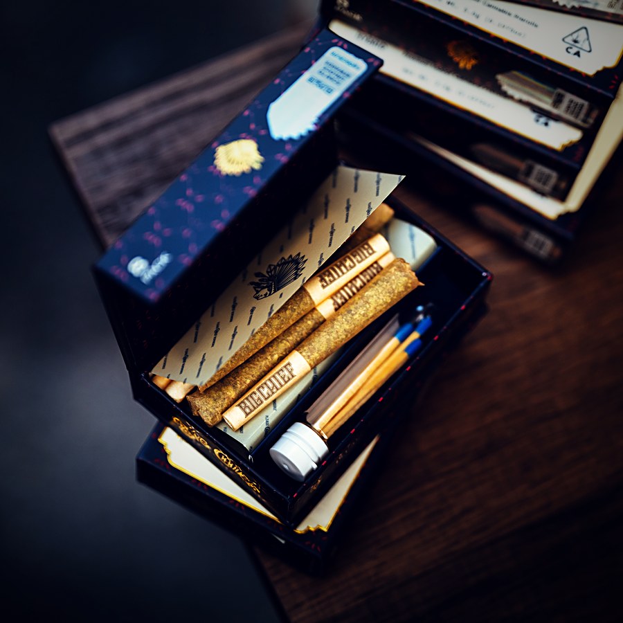 Open Big Chief preroll boxes and gold-dusted prerolls on a wood table